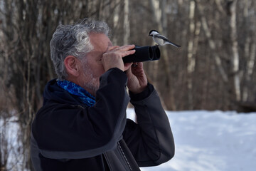 Black Capped Chickadee sitting on the binoculars of a bird watcher.  Humorous and unexpected portrait!