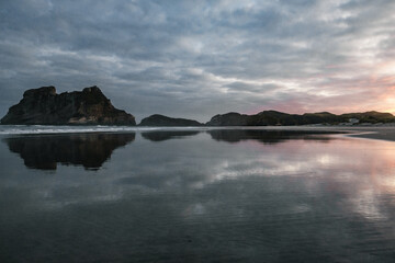 Calm water reflecting rocks and a subtle sunrise in the background.