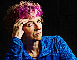 Color portrait of a middle aged woman leaning on her hand, with a serious expression and pink hair.