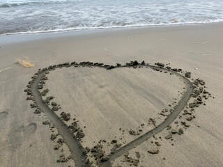 Love heart drawn in the sand on a beach with a wave coming to wash it away