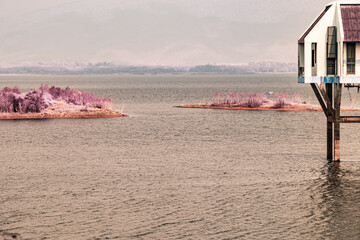 An infrared style, a body of water with two small islands and a building is on stilts over the water