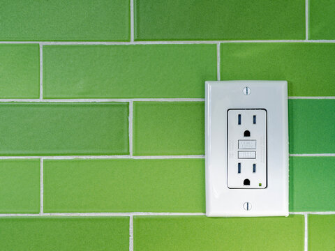 A GFCI (Ground Fault Circuit Interrupter) electrical outlet on a green tiled wall