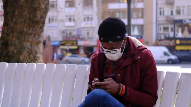 African Teenager Looking at his Phone in the Park