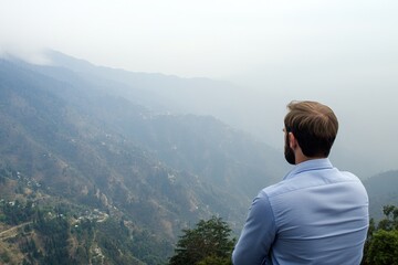 A man gazes at a misty mountain landscape, reflecting on nature's beauty and tranquility.