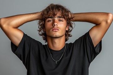A young man poses confidently with hands behind his head, showcasing a relaxed and stylish look.