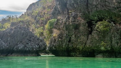 Picturesque karst cliffs in the emerald lagoon. Green tropical vegetation on steep slopes. Blue...