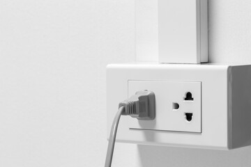 Plug from an electrical appliance. plugged into an electrical outlet on white wall background.