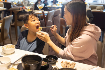 Happy Young Mother Feeding Her  Son in Restaurant