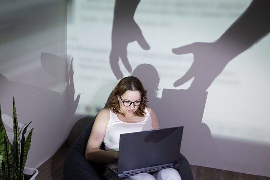 A woman experiences various online threats while she is using her laptop in a dimly lit environment that feels unsafe - Powered by Adobe
