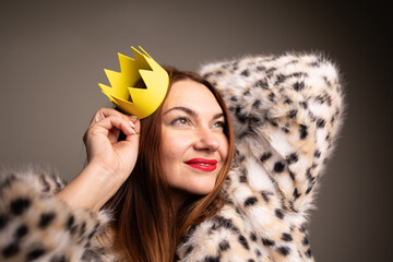 A stylish woman in a luxurious faux fur coat and a playful yellow crown, radiating confidence and joy