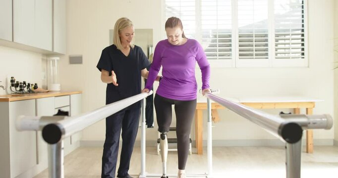 Woman in prosthetic leg walking with therapist on parallel bars in clinic