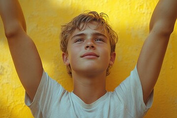 A young boy with arms raised, smiling against a vibrant yellow wall, conveying joy and freedom.