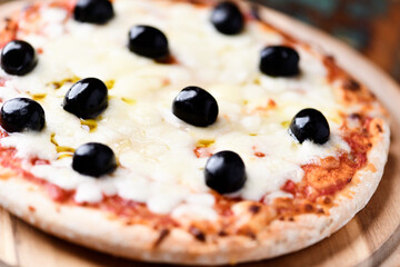 Pizza with mozzarella cheese and black olives on wooden background. Soft focus. Close up	