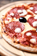 Pizza with salami and mozzarella cheese. Wooden background. Soft focus. Close up.