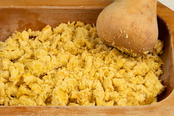 Mashed boiled plantains in a wooden bowl with a wooden pestle, creating a traditional green plantain mash, a cultural tropical dish, widely enjoyed in Latin American and Caribbean cuisine. © Octavio