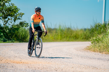 Fototapeta premium Bicyclist riding along a gravel path under a clear blue sky in warm weather