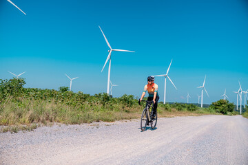 Obraz premium Cyclist rides along a gravel path surrounded by wind turbines on a clear day