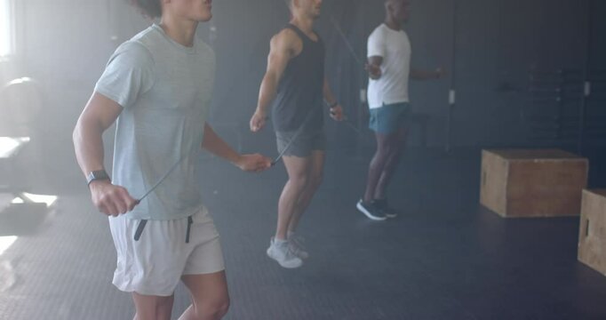 Group of diverse men training with jump ropes in gym, wearing athletic clothing