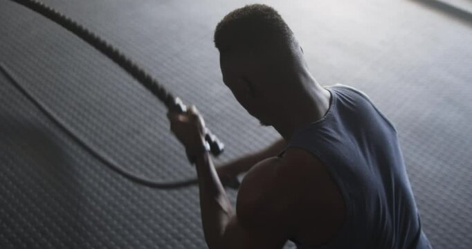 Using battle ropes, man exercising in gym for strength training workout