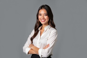 Confident Young Professional Woman in a White Shirt Posing with Crossed Arms on a Plain Gray Background for Corporate and Personal Branding Use