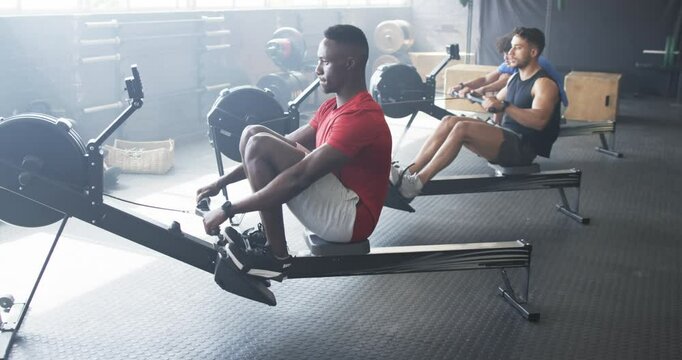 Group of diverse young men training on rowing machines in gym