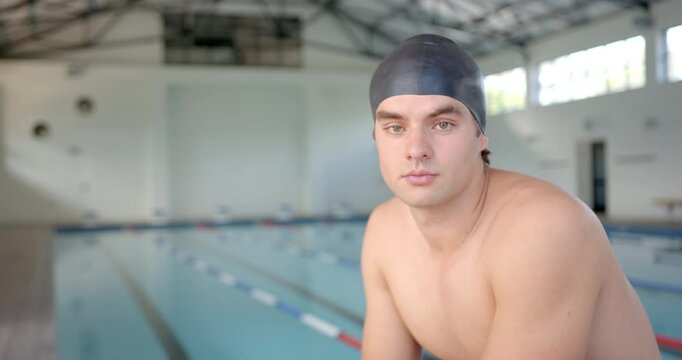 male swimmer wearing swim cap posing by indoor pool, preparing for training session, copy space