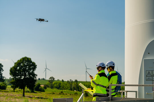 Engineers monitor drone operations at a wind farm site in bright daylight with wind turbines in the background