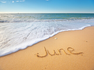 June word written on sea sand shore beach at day.
