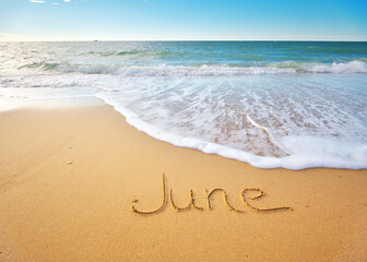 June word written on sea sand shore beach at day.