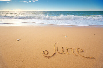 June word written on sea sand shore beach at day.