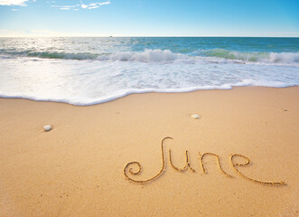June word written on sea sand shore beach at day.
