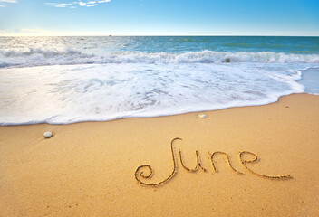 June word written on sea sand shore beach at day.