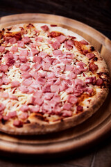 Pizza with ham and mozzarella cheese on wooden background. Soft focus. Close up