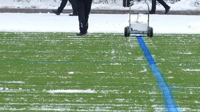 the manager of the football stadium draws a blue line with line marking machine on the field in winter