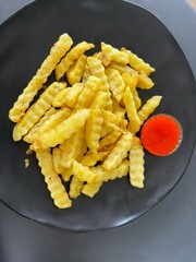 Close-up of crispy golden French fries served on a black plate with a dollop of red chili sauce, emphasizing the texture and delicious appeal. Perfect for food and culinary themes