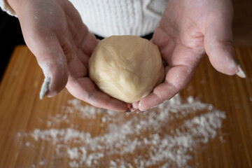 Hands holding fresh dough on a floured wooden surface