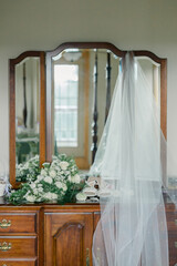 Bridal veil, bouquet, and shoes displayed on a vintage wooden dresser.