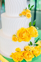 White three-tiered wedding cake adorned with yellow roses.
