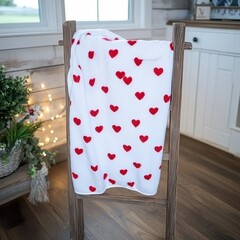 Cozy blanket with red hearts displayed on a wooden rack.