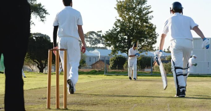 Two teams of multiracial male cricket players playing cricket, batters running with bats on pitch