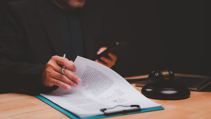 Legal professional examines important documents while holding smartphone, surrounded by gavel and...