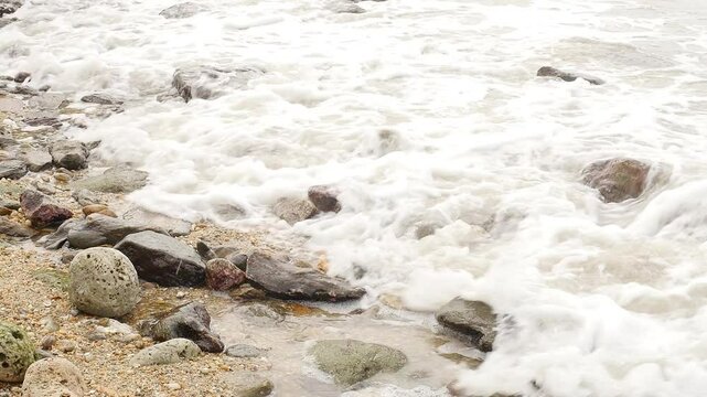 Foamy Waves Crashing on a Rocky Shoreline: A Close-Up View of the Ocean&rsquo;s Dynamic Movement, Showcasing the Natural Power and Beauty of Water Interacting with Rugged Coastal Rocks
