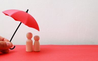 Couple of wooden figures of a man and a woman covered by an red umbrella. the concept of husband...