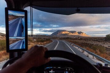 View from the driver's seat of a truck on a conventional road with a mountain landscape and clouds...