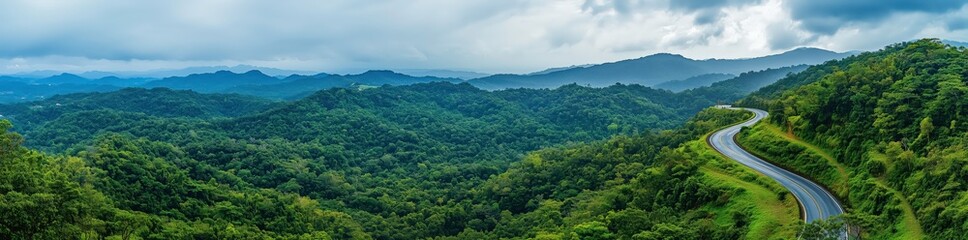 Fototapeta premium Mountain Road through Lush Landscape: A winding road snakes its way through a vibrant green mountain landscape, clouds drifting over the peaks in a breathtaking panorama. 