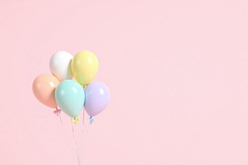 Five semi transparent balloons with ribbons in pastel colors on a light pink background