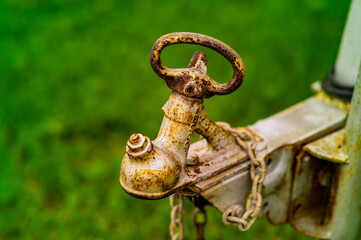 Close up of an old rusty steel trailer coupling with safety chain attached to a boat trailer against green background