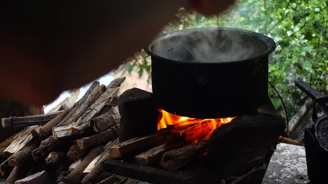 In a simple and old-fashioned way, cooking food with a stainless steel pot and an Anglo charcoal stove. to get a dark sooty color over a long time. The charcoal stove has a red light on it.