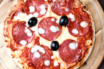 Pizza with salami and mozzarella cheese. Wooden background. Soft focus. Top view. Close up	