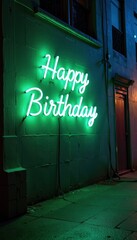 Naklejka premium Happy Birthday written in a glowing green and blue neon style, radiating against a dark urban alley wall.
